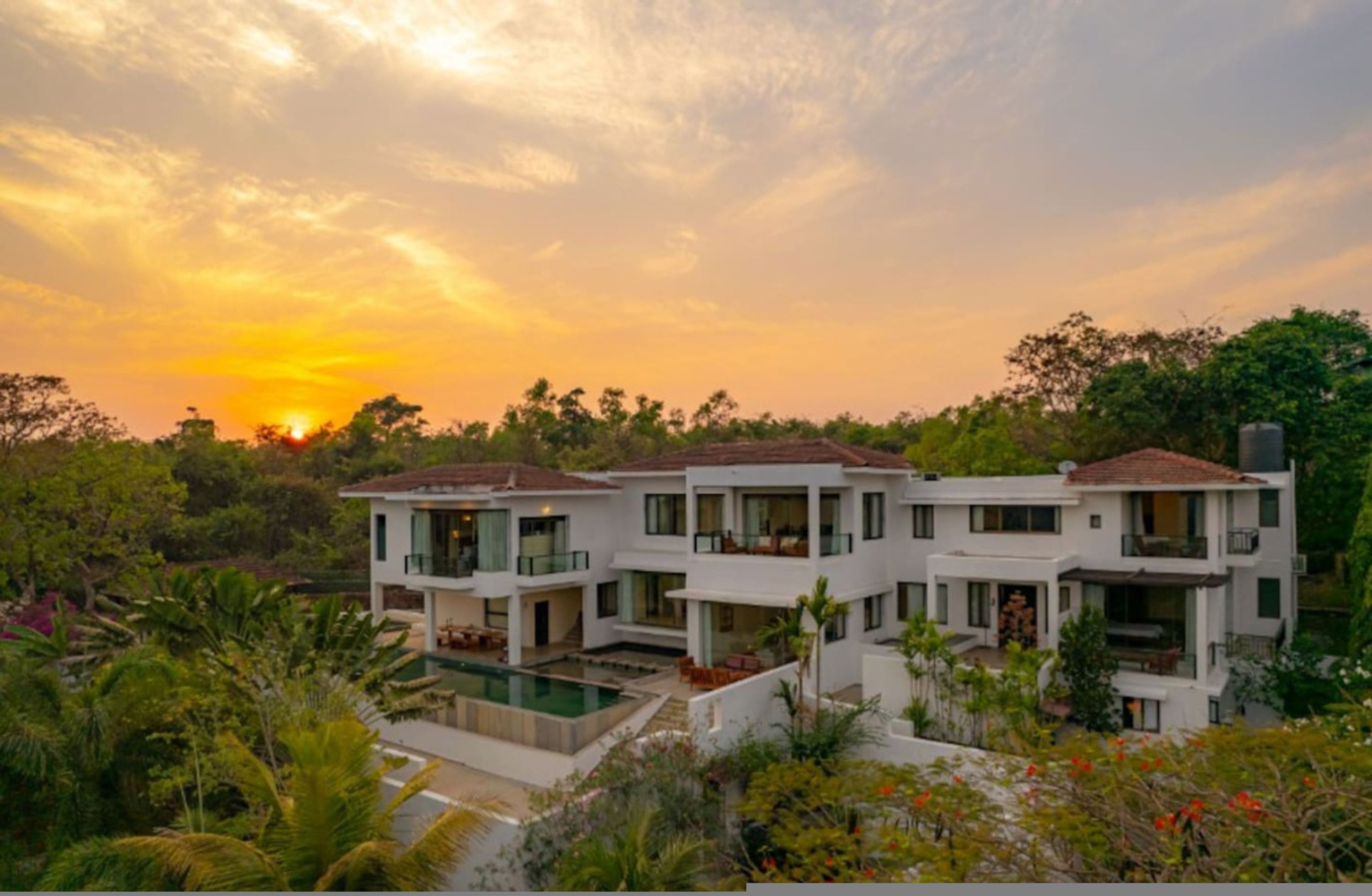 A modern multi-story house with a swimming pool, surrounded by lush greenery and trees.
