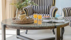 Een gestreepte fauteuil met een glazen tafel ervoor, een potplant en een glas sinaasappelsap.