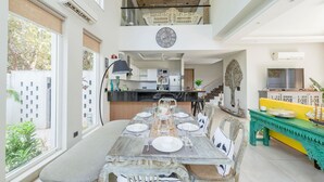 Een ruime eethoek met een hoge plafond, een keuken op de achtergrond en een balkon met decoratieve balustrade.