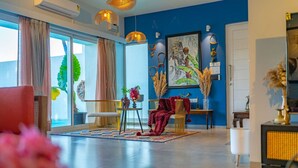 A modern living room with a large window, a blue accent wall, and a variety of decorative items. - Legacy by Hireavilla Natgeo Spot w Field Views (Siolim)