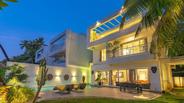 A modern two-story house with a swimming pool, outdoor seating, and a well-lit balcony. - Legacy by Hireavilla Natgeo Spot w Field Views (Siolim)