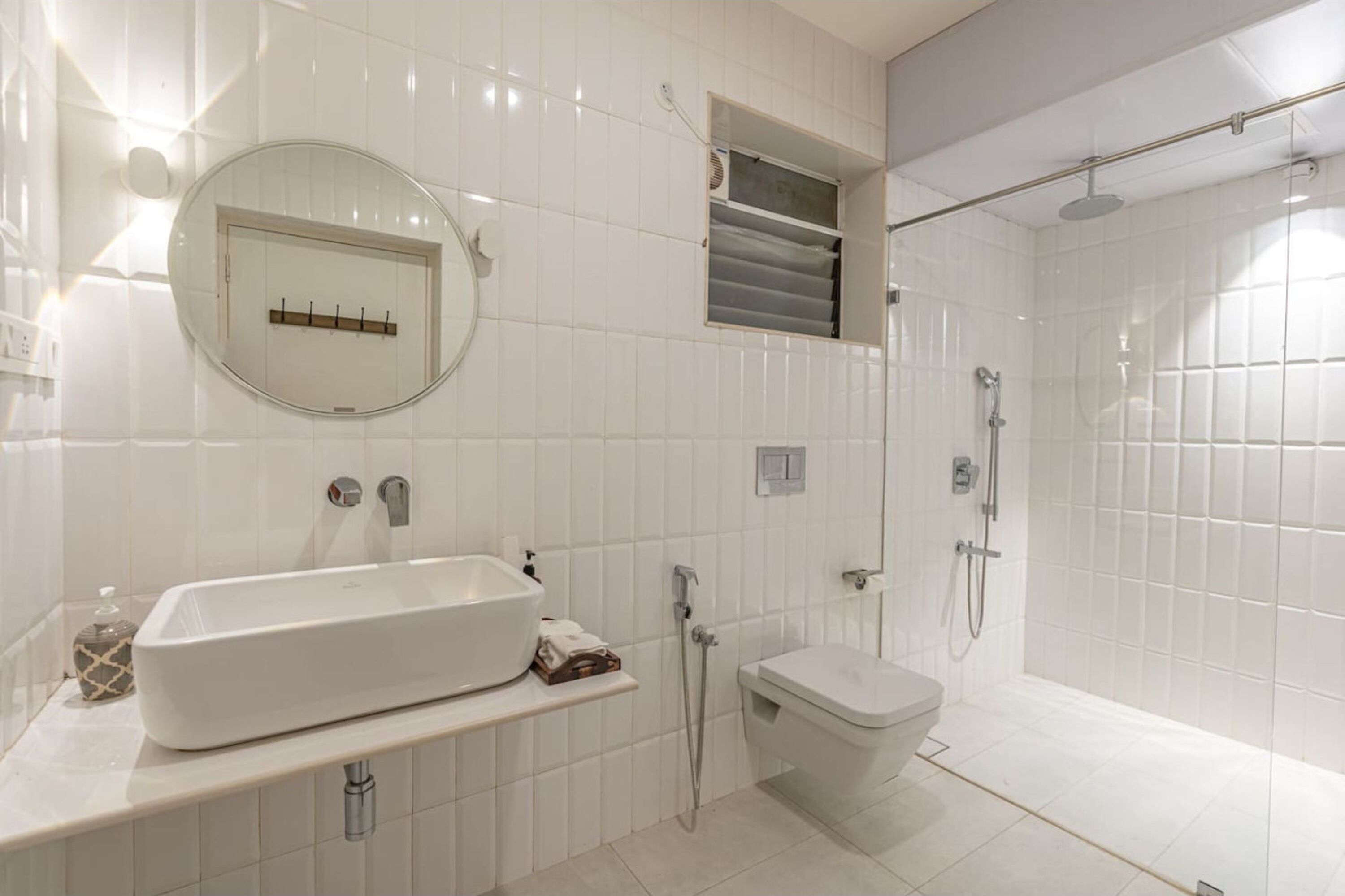 A modern bathroom with a large white sink, a round mirror, a toilet, and a shower area.