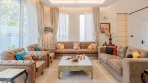 A spacious living room with a beige sofa set, a coffee table, and a ceiling fan. - Lux 5BR Villa in Anjuna Perfect for Groups Aria (Anjuna)