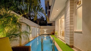A swimming pool with a glass table and chair, surrounded by artificial grass and a wicker chair. - Lux 5BR Villa in Anjuna Perfect for Groups Aria (Anjuna)