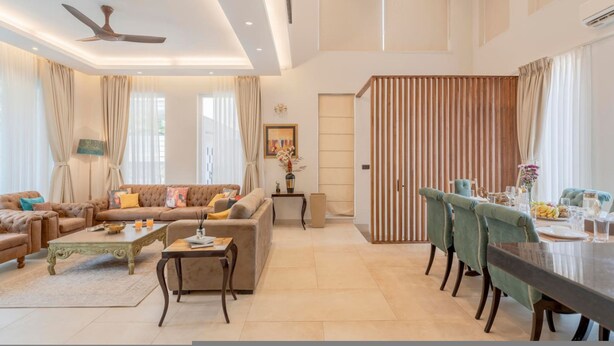 A spacious living room with a sofa, coffee table, and dining area with chairs and a table set for a meal. - Lux 5BR Villa in Anjuna Perfect for Groups Aria (Anjuna)