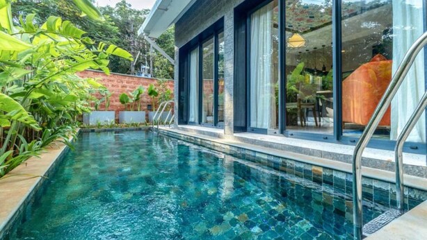 Une piscine dont le bord est revêtu de carreaux, entourée d’un mur de briques et d’une végétation luxuriante.