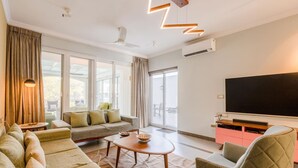 Una sala de estar moderna con un conjunto de sofás, una mesa de centro, un televisor y un ventanal grande.