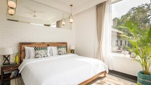 Ein Hotelzimmer mit einem großen Bett, einem hölzernen Kopfteil, einem großen Fenster mit Blick auf Grünflächen und einer Topfpflanze auf dem Fensterbrett.