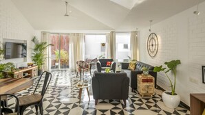 A modern living room with a black and white checkered floor, a flat-screen TV, a sofa, a coffee table, and a dining area with a wooden table and chairs.