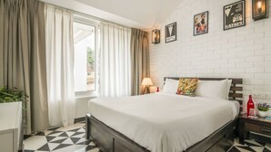 A hotel room with a large bed, a white brick wall, and a window with curtains.