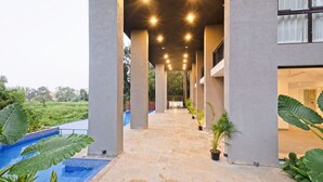 A covered walkway with a pool, columns, and potted plants. - Cozy 1BR With Pool - Only 1km From Candolim Beach (Candolim)