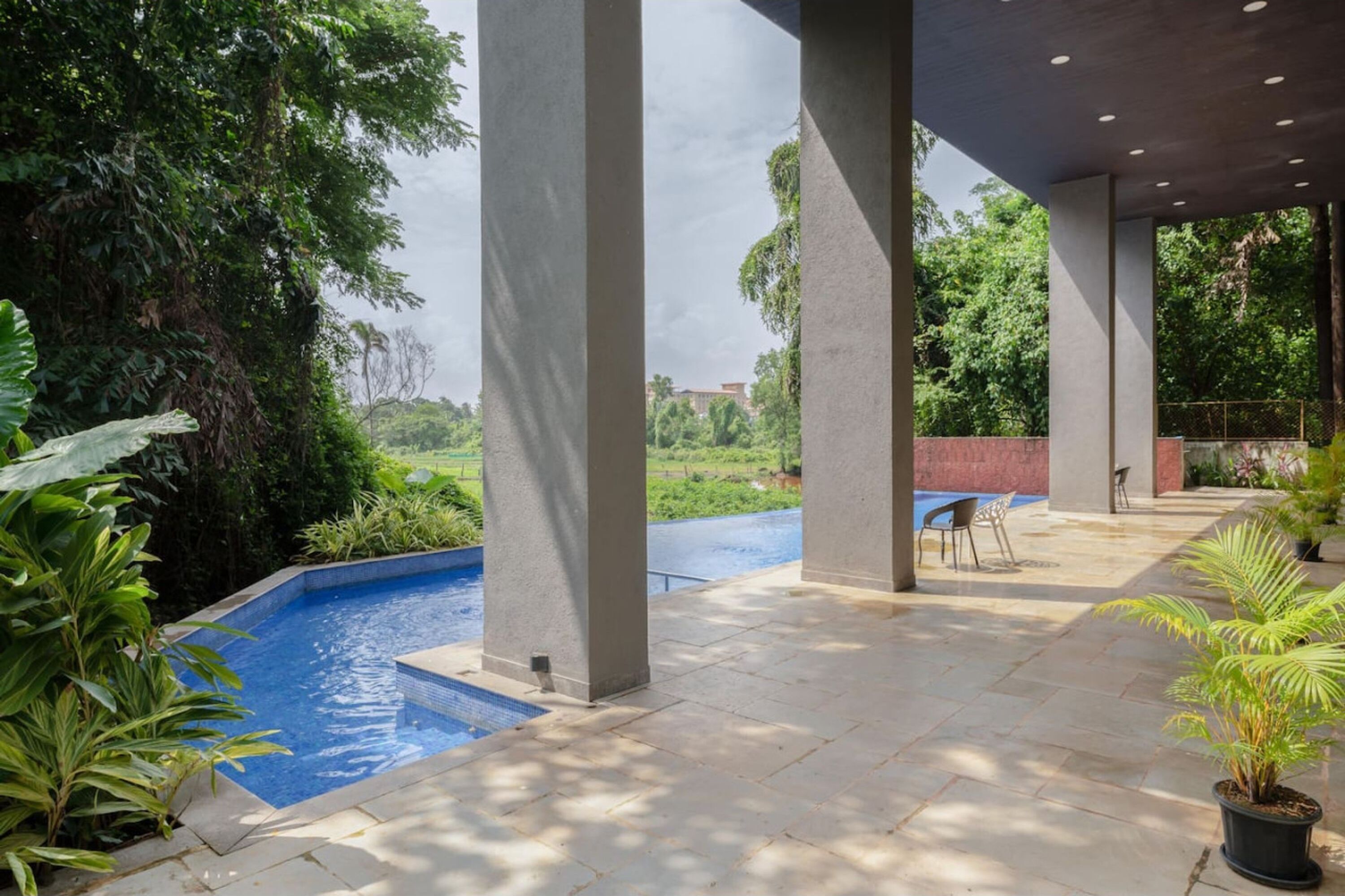 A covered outdoor area with a swimming pool, surrounded by greenery and columns.