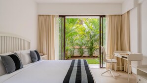 A modern hotel room with a large bed, a desk, and a view of a lush garden. - Cozy 1BR With Pool - Only 1km From Candolim Beach (Candolim)