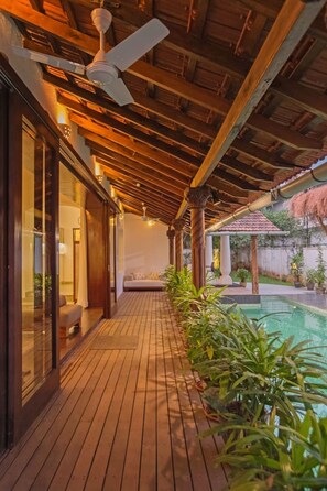 A wooden deck with a ceiling fan, a pool, and potted plants. - Salt by Hireavilla - 4BR w Heated Pool in Siolim (Siolim)