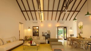 A spacious living room with a high ceiling, a dining area with wooden chairs, and a sofa set. - Salt by Hireavilla - 4BR w Heated Pool in Siolim (Siolim)