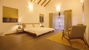 A bedroom with a bed, bedside tables, a chair, and a window with curtains. - Salt by Hireavilla - 4BR w Heated Pool in Siolim (Siolim)