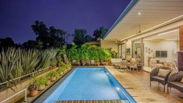 Una piscina rectangular con paredes de azulejos, rodeada de plantas en macetas y una terraza de madera.