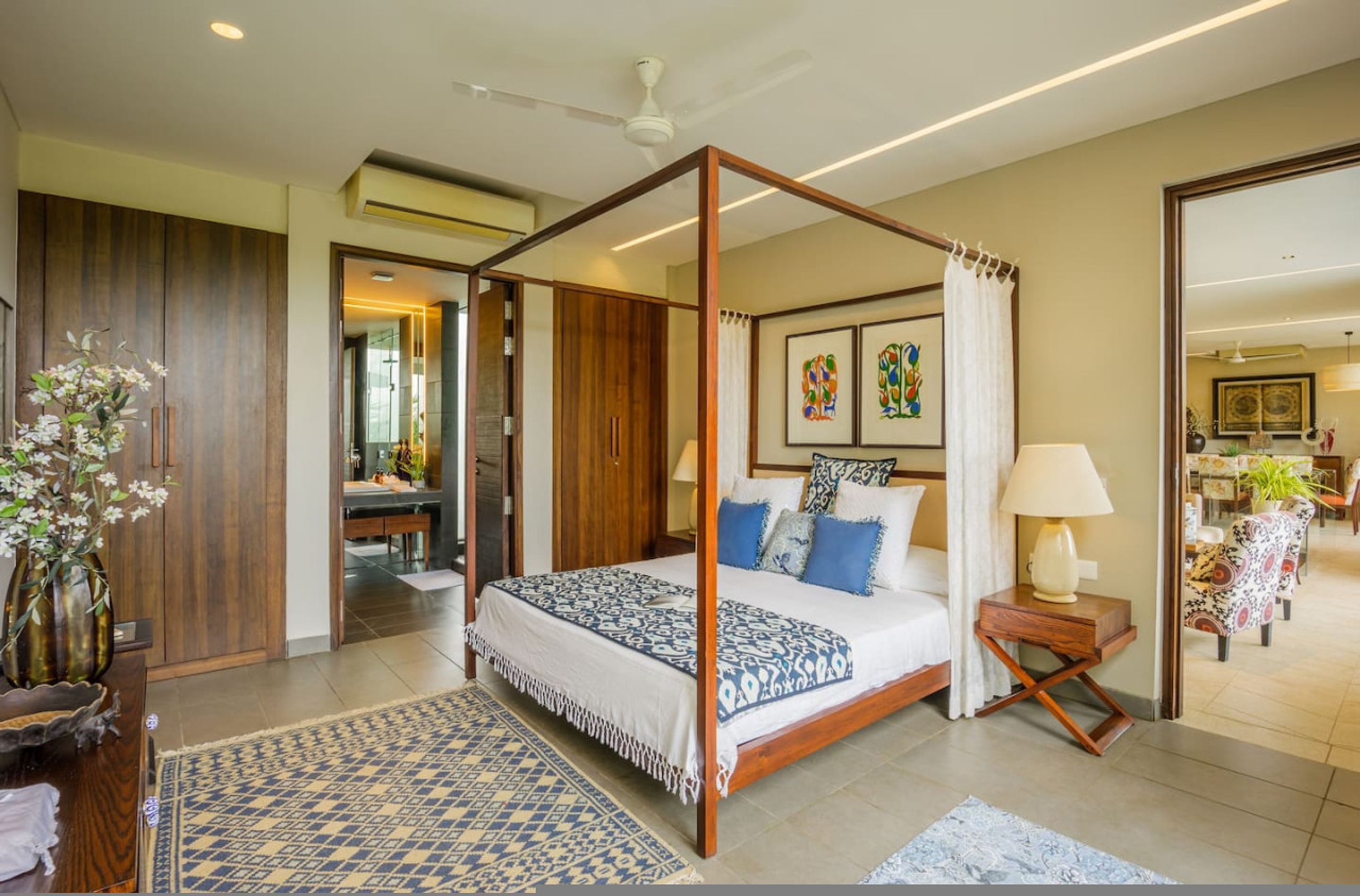 A four-poster bed with a patterned bedspread, a wooden floor, and a view into the adjacent room.