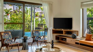 Un soggiorno moderno con televisione, sedute confortevoli e vista su piscina e vegetazione.