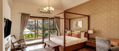 A four-poster bed with a wooden frame, a ceiling fan, a chandelier, a television, a rocking chair, a desk, and a chair.