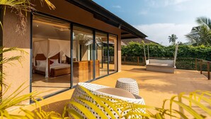 A modern hotel room with a glass wall, a bed, a sitting area, and a balcony with plants. - Puravida I -luxury 5bhk w Pvt Pool in Anjuna (Anjuna)