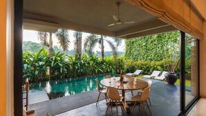 A modern outdoor dining area with a pool, surrounded by lush greenery and palm trees. - Puravida I -luxury 5bhk w Pvt Pool in Anjuna (Anjuna)