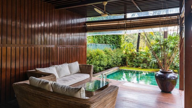 Ein moderner Außenbereich mit einer Rattan-Couch und einem Glastisch, mit Blick auf einen Pool und üppiges Grün.