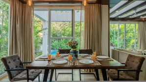 A dining area with a table set for four, surrounded by curtains, with a view of greenery outside. - Luxe 3bhk w Private Pool Assagao Casa Rehmyra (Assagao)