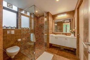A bathroom with a glass shower enclosure, a toilet, a sink with a mirror, and patterned tiles. - Sol Banyan by Hireavilla - 1BR w Pool in Candolim (Candolim)