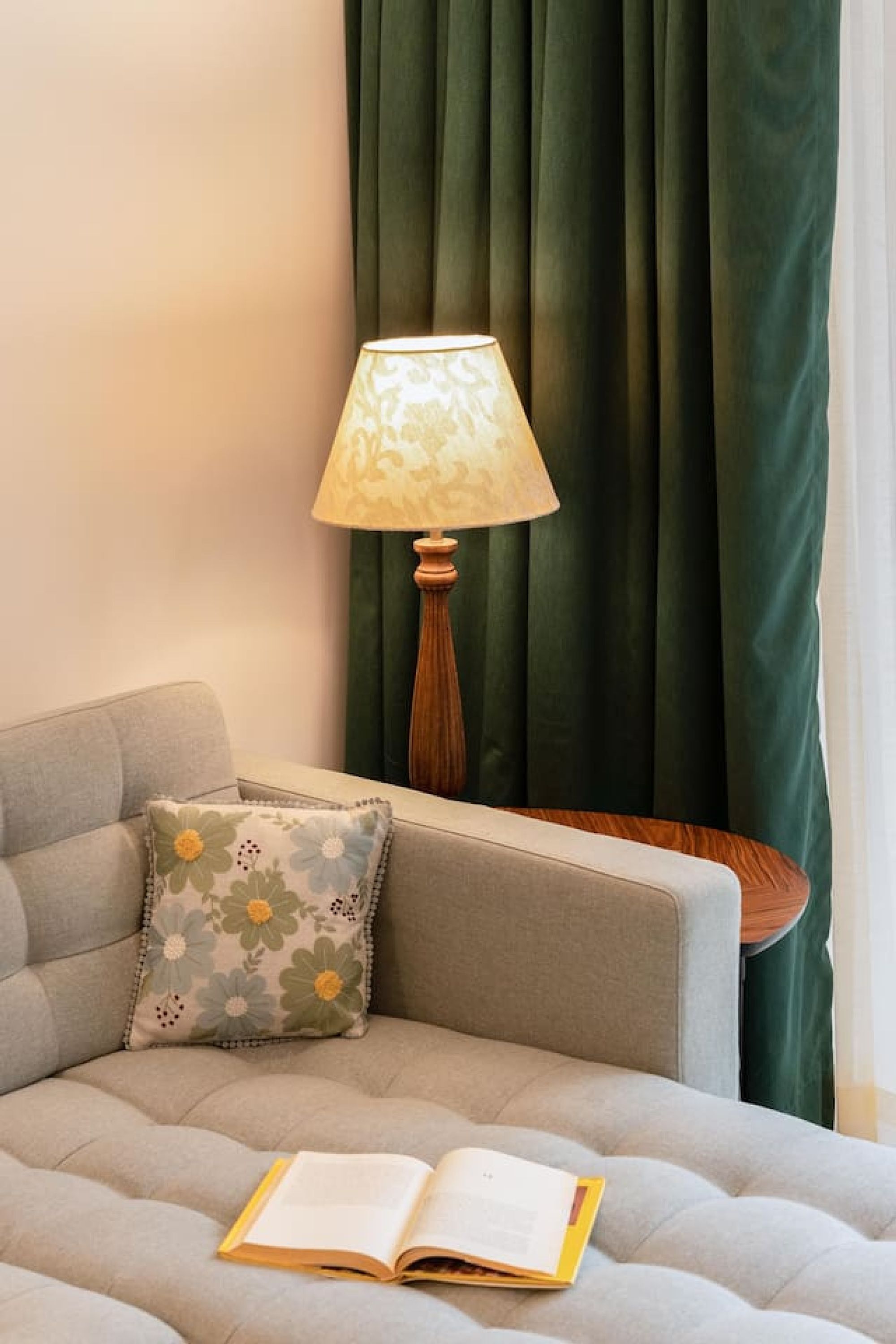 A cozy room with a grey sofa, a floral pillow, a wooden floor lamp, and an open book on the sofa.