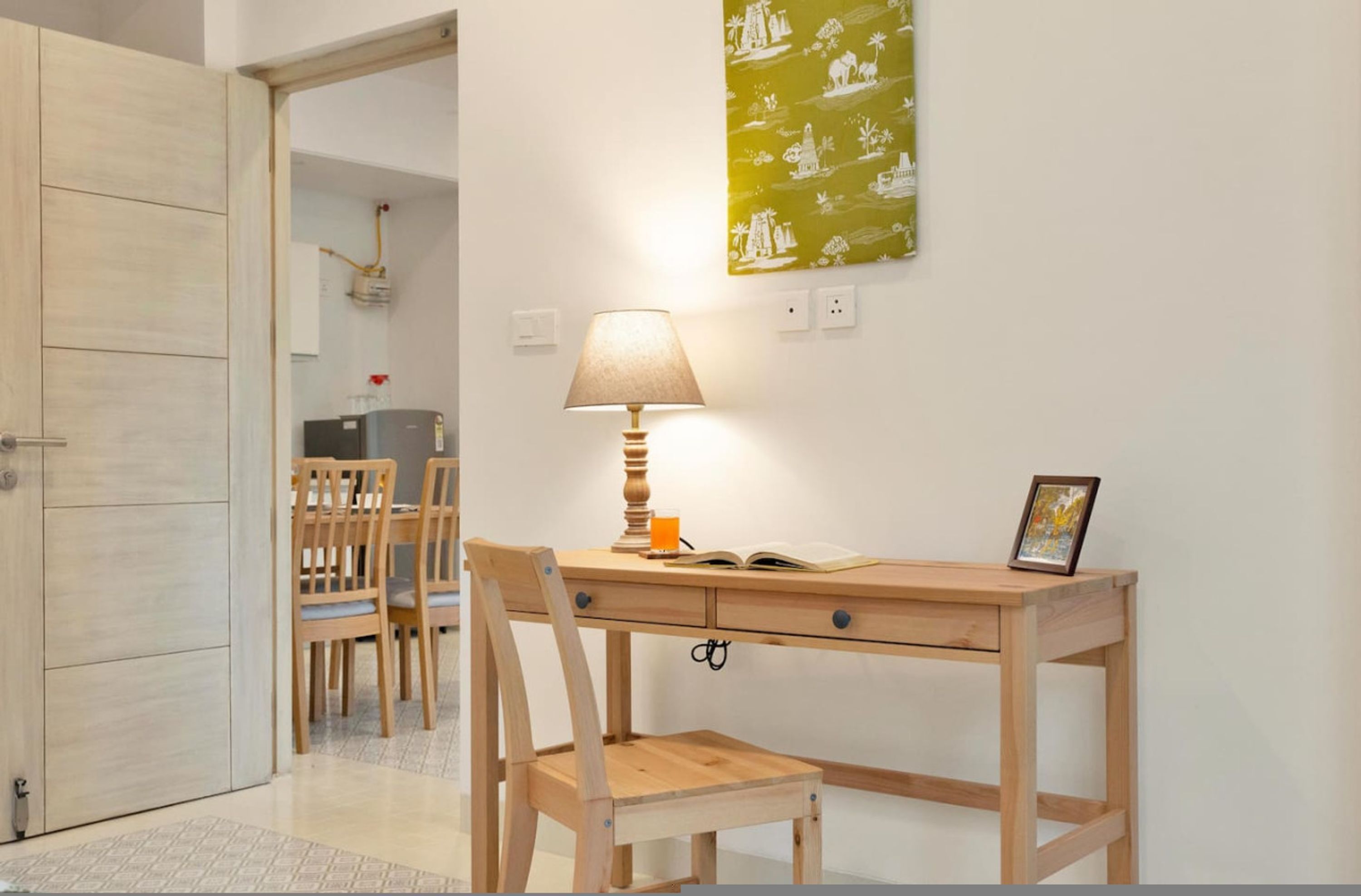 Un bureau en bois, une lampe, une chaise et une petite table sur laquelle se trouvent un cadre photo et un livre.