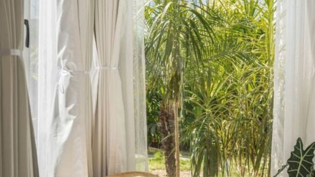 A room with a view of a garden through sheer curtains, a woven ottoman, and patterned flooring. - Nova by Hireavilla - 2BR w Private Pool in Anjuna (Vagator)