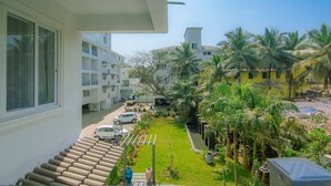 A residential building with a balcony overlooking a well-maintained garden with palm trees and a clear sky. - Luxe Apt w Balcony Rooftop Pool 15 min to Beach (Marra)