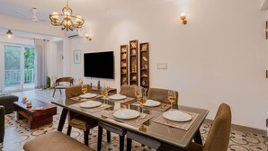 A dining area with a table set for four, a chandelier, and a flat-screen TV mounted on the wall. - Luxe Apt w Balcony Rooftop Pool 15 min to Beach (Marra)