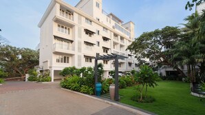 A multi-story residential building with balconies, a covered walkway, and a well-maintained garden. - Luxe Apt w Balcony Rooftop Pool 15 min to Beach (Marra)