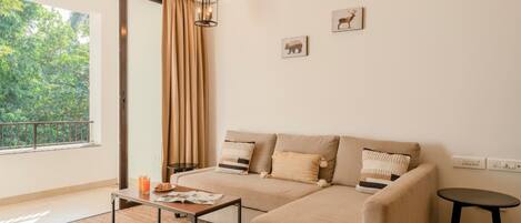 A modern living room with a sofa, a coffee table, and a small table. There is a window with curtains, a wall-mounted air conditioner, and a picture of a deer.