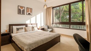 Un dormitorio con una cama grande, una mesita de noche, una silla, un ventilador de techo y una ventana con cortinas.