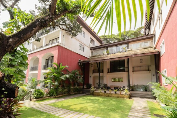 A building with a red facade, a covered patio area with outdoor seating, and a well-maintained garden with various plants and a pathway.