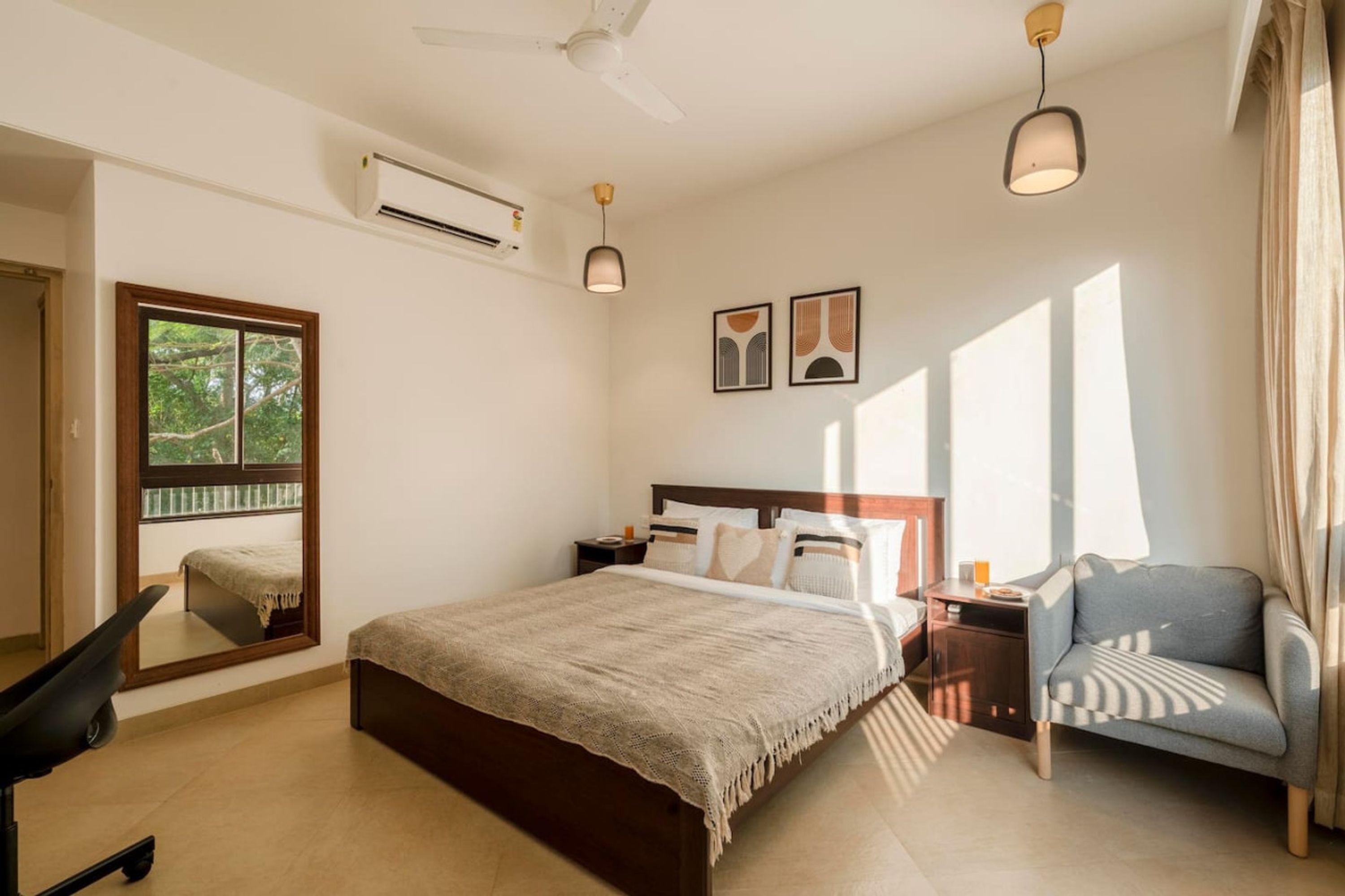 A bedroom with a bed, a chair, a nightstand, a mirror, and a window.