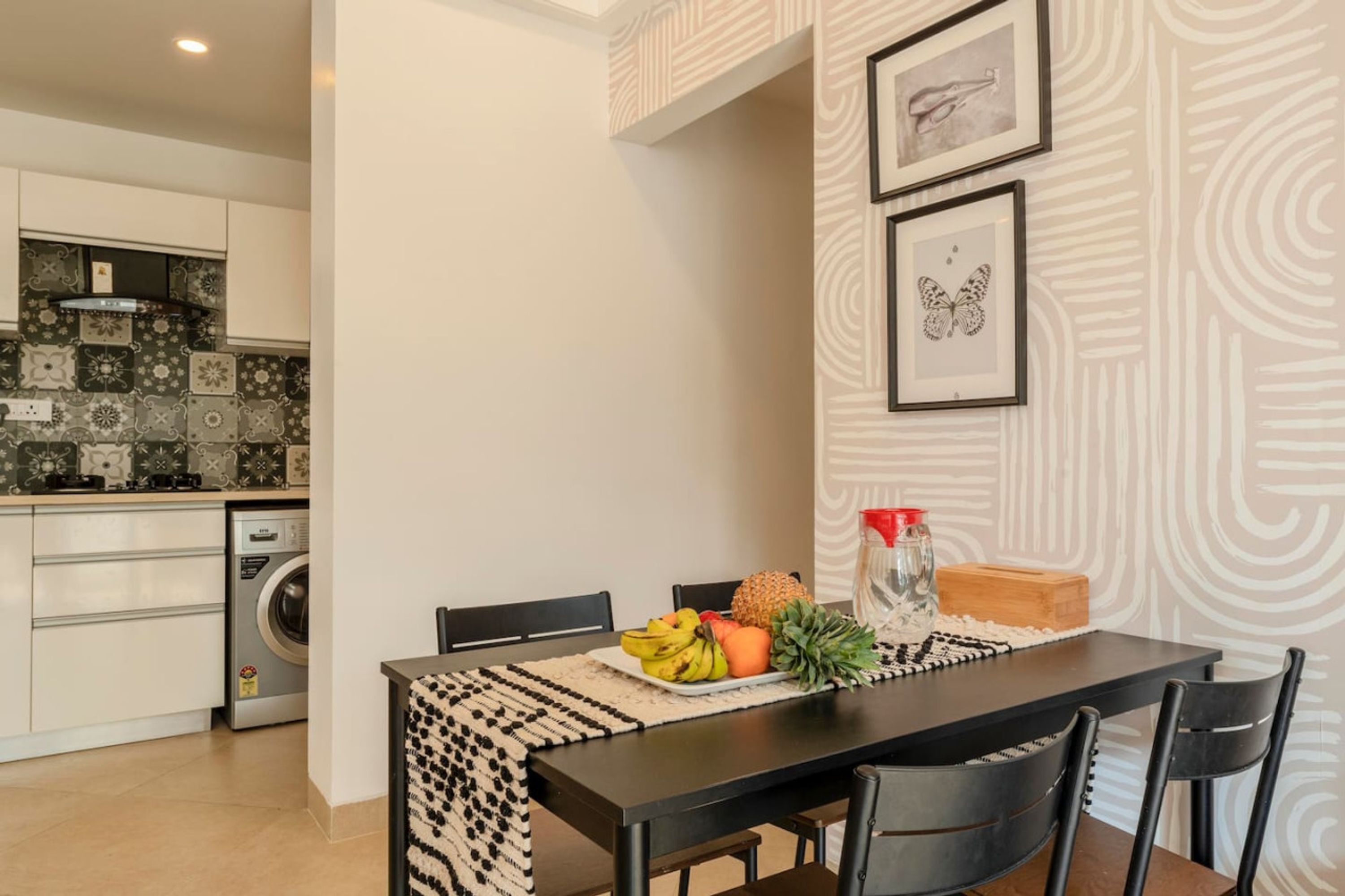 Una cocina moderna con armarios blancos, una lavadora y un comedor con una mesa y sillas negras.
