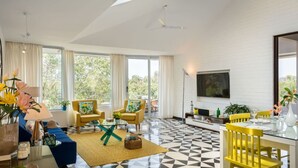 Una sala moderna con piso de estampado geométrico, un sofá, sillas amarillas, una mesa de comedor con sillas amarillas y un televisor montado en la pared.