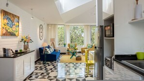 Una cocina moderna con refrigerador, un comedor con mesa y sillas, y una sala de estar con sofá y mesa de centro.