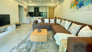 A modern living room with a sectional sofa, a coffee table, and a TV. - Cozy 1BR in Candolim - Walking Distance to Beach (Candolim)