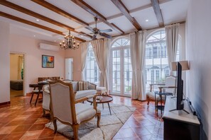 A spacious living area with a high ceiling, exposed wooden beams, a chandelier, and large windows with curtains. - Casa Del Leon by Hireavilla -3br w Pool in Assagao (Assagao)