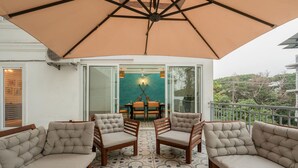 A covered outdoor seating area with cushioned chairs and a table, a ceiling fan, and a view of a dining area through glass doors.