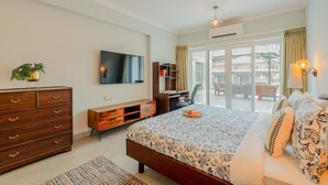 A bedroom with a bed, dresser, TV, and a balcony with a view.