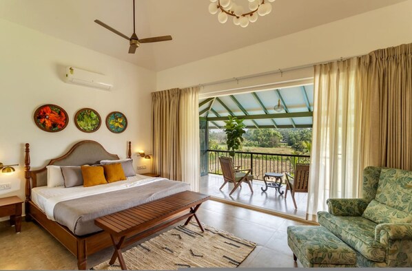 A bedroom with a bed, bedside tables, a ceiling fan, and a view of an outdoor balcony with chairs and a table.