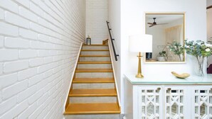Un escalier avec des murs en briques blanches, une main courante en bois et une console en verre sur laquelle sont posés une lampe et des objets décoratifs.