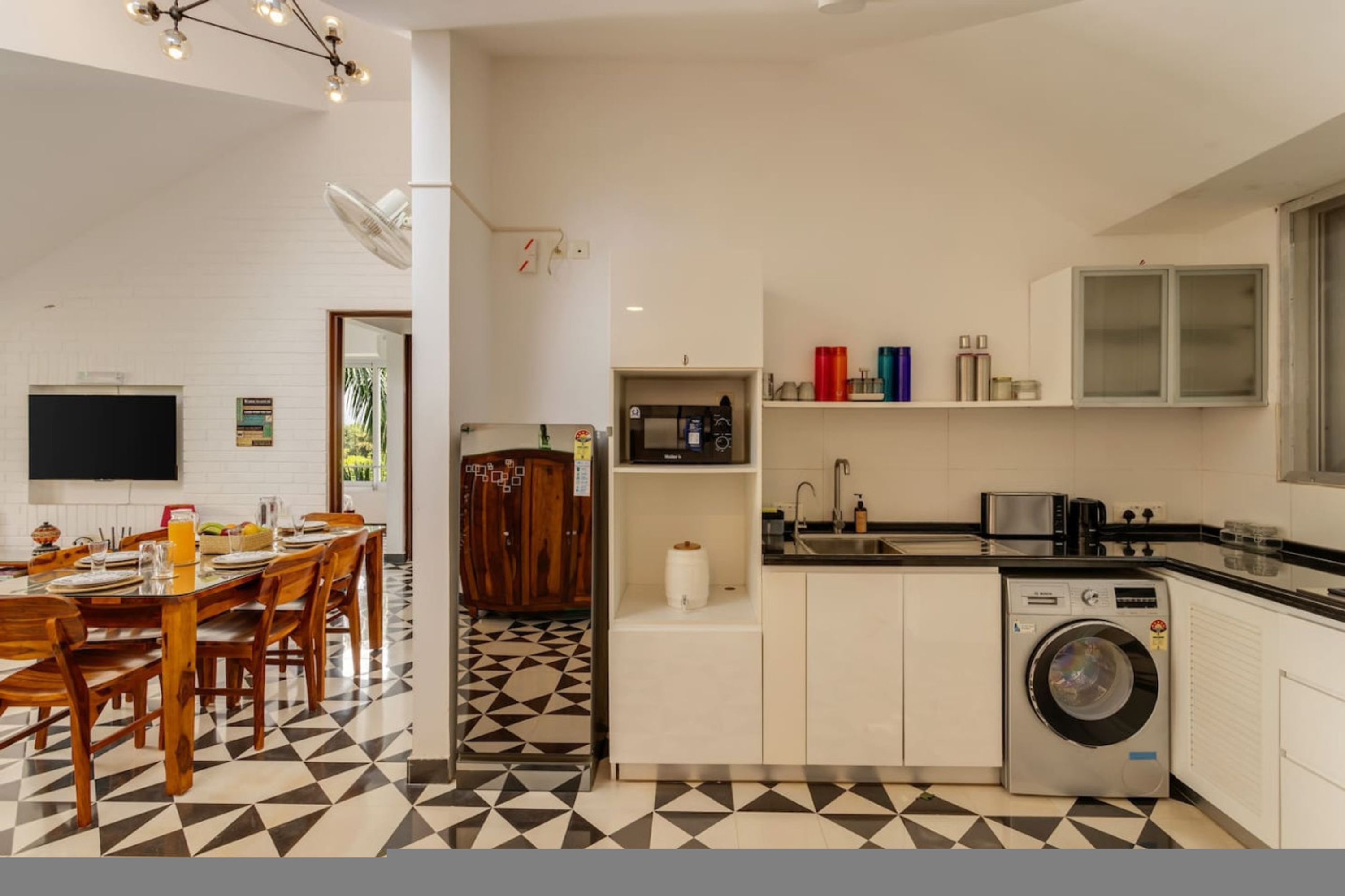 Una cocina moderna con lavadora, un comedor con mesa lista y un televisor montado en la pared.