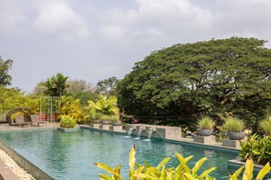 A rectangular pool with a waterfall feature, surrounded by potted plants and trees. - 2BR w Rooftop Pool in North Goa Close to Beaches (Nerul)